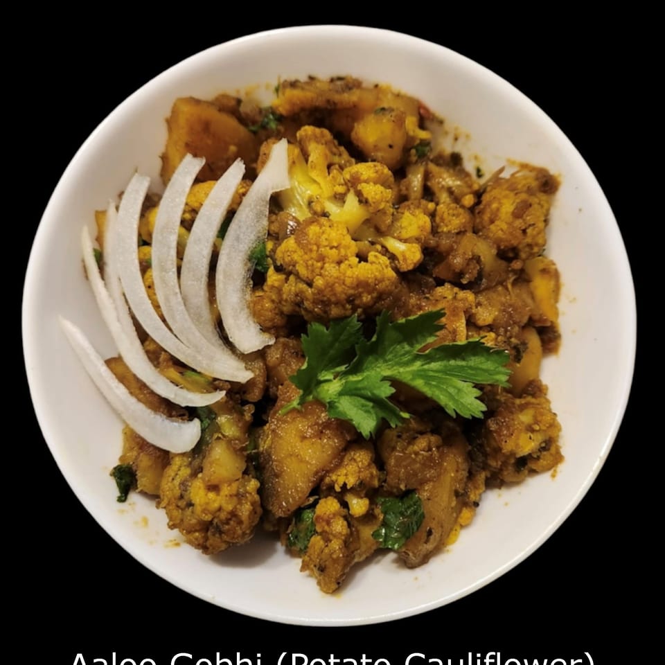 A plate of golden aloo gobi, featuring spiced potatoes and cauliflower garnished with sliced onions and fresh cilantro.
