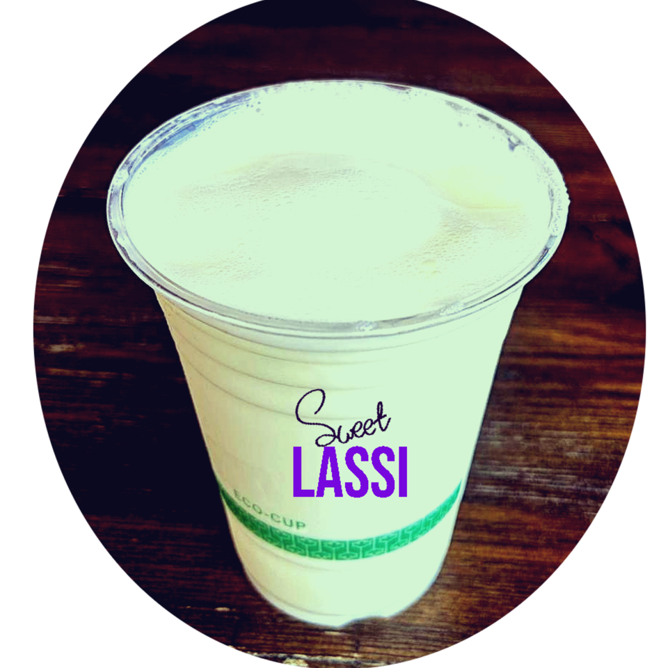 A creamy dessert in a branded cup labeled “Sweet Lassi,” displayed on a dark wooden table.