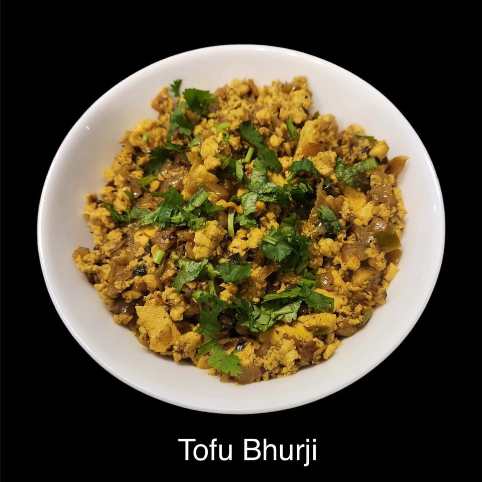Tofu bhurji with crumbled golden tofu, onions, spices, and fresh cilantro served in a white bowl against a black background.